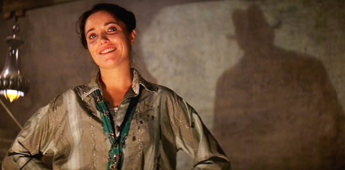 Marion fait face à Indiana Jones, dont seul son ombre se marque sur le mur derrière elle.