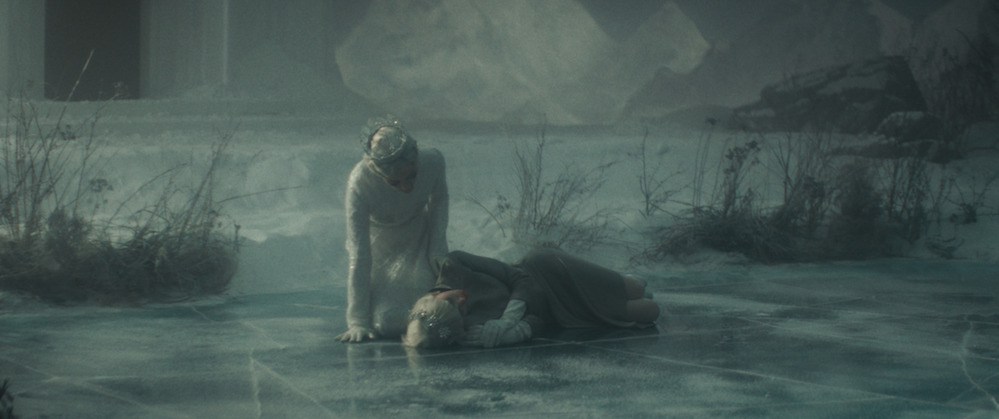 Au-dessus de Jeanne, La Reine des neiges et penchée, au milieu de ce qui semble être un début de blizzard dans ce grand studio de tournage.