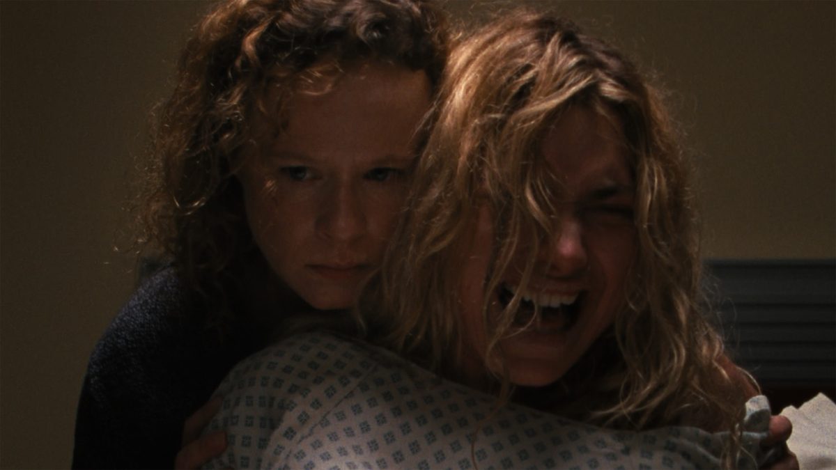 Lidia (Imogen Poots) en pleine crise de pleurs et vêtue modestement d'une robe d'hôpital est maintenu par sa grande soeur qui tente de lui apporter son soutien au vu de l'épreuve difficile qu'elle vit. Le plan est rapproché. Image de The Chronology of Water. 