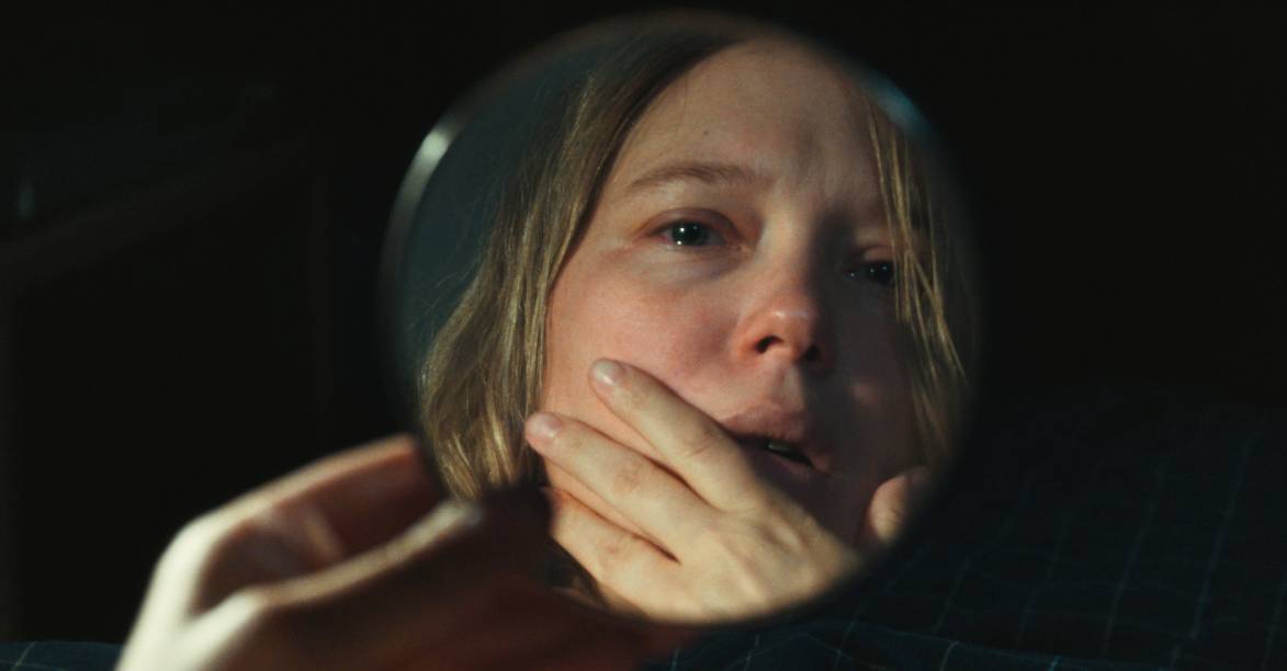 David Zimmerman, dans le corps de L'inconnue découvre avec terreur sa nouvelle enveloppe corporelle dans le reflet d'une petit miroir circulaire portable. Image issue du film L'inconnue